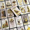 A spread of illustrated tarot cards from Schiffer Publishing, Ltd.’s Shadowland Lenormand deck features whimsical, spooky art—like the fox, mountain, and owl—plus a central Shadowland Lenormand booklet, perfect for shadow work or cartomancy.