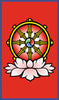 A golden Dharma wheel with eight spokes, symbolizing enlightenment, stands above a white lotus on red bordered in blue. The wheel's center has a blue, red, and green swirl evoking The Buddha Tarot by Schiffer Publishing, Ltd.