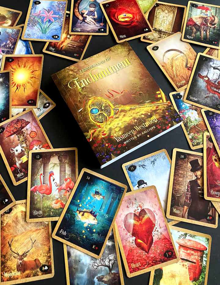 A deck of vibrant Lenormand of Enchantment cards by Schiffer Publishing, Ltd. is spread out with its guidebook, showing animals, flowers, fantasy scenes, and symbols on a dark surface.