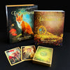 The Lenormand of Enchantment deck set by Schiffer Publishing, Ltd. showcases Yasmeen Westwood’s enchanting illustrations and a fox on the box, with three cards, a guidebook, the deck, and two boxes shown on a black surface.