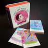 A box of Dream Your Joy Oracle Cards by Schiffer Publishing, Ltd. sits beside three colorful affirmation cards with whimsical, Mind Painting-inspired illustrations and positive messages, all arranged on a black background.