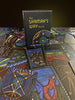 A box labeled The Shaman’s Way Oracle by Schiffer Publishing, Ltd. stands upright on illustrated oracle cards, all featuring intricate mystical symbols and vibrant spiritual artwork designed for spiritual healing.