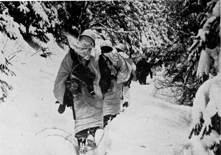 Soldiers featured in "Dying Hard" by Schiffer Publishing, Ltd. march in white camouflage through snowy woods during WWII, seamlessly blending into the wintry forest like true brothers in arms.