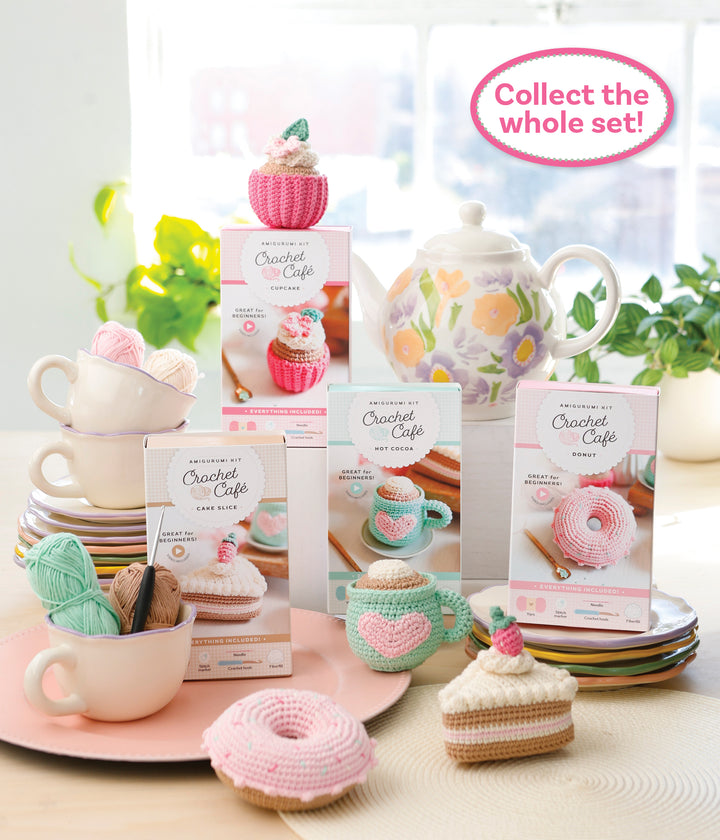 A display of Schiffer Publishing, Ltd.’s Crochet Cafe Amigurumi Kit Donut sits among pastel dishes, yarn, and a teapot. Text in a pink bubble says, "Collect the whole set!.
