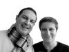 Two adults smile at the camera against a white background, their looks inspired by "10 Innovations That Will Shape Tomorrow's Architecture" from Schiffer Publishing, Ltd.—one in a checkered scarf and light sweater, the other in a dark top with short hair.