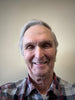 An older man with gray hair smiles at the camera in a plaid shirt against a plain backdrop, echoing the style of barns featured in "The Historic Dutch American Barns of New Jersey and Southern New York" by Schiffer Publishing, Ltd.