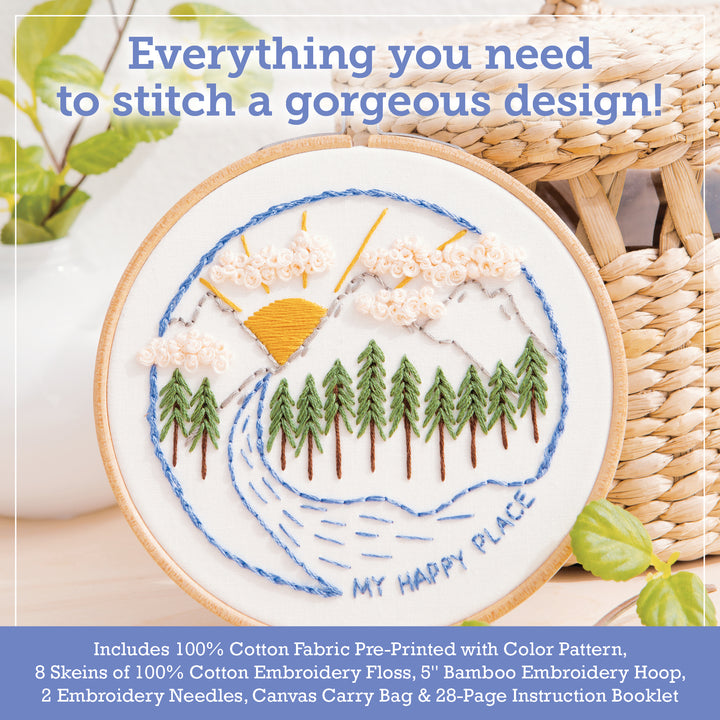 The Sunny Stitches Embroidery Kit Sunshine Pines by Schiffer Publishing, Ltd. features a hoop with a hand-embroidered mountain landscape and "MY HAPPY PLACE" text. Includes materials, with a woven basket in the background.