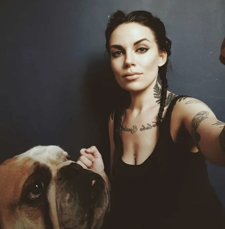 A woman with braided hair and tattoos takes a selfie with an Oracle of the Mythical Ocean tarot set next to an English bulldog.