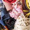 Close-up of colorful recycled materials like fabric scraps, twine, and rope arranged on a white surface with "Weaving" by Schiffer Publishing, Ltd. on the right, highlighting sustainable weaving practices.