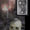 I. Lucifer by Schiffer Publishing, Ltd. is displayed with a human skull adorned with a black feather, three lit candles, and a framed sculpture of a pregnant figure with a crescent moon against a dark backdrop.