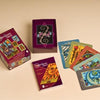 The Otherworld Tarot deck, displayed on a beige surface, includes an open box, a Tarot reading guide booklet, and several vividly illustrated cards artfully spread out.
