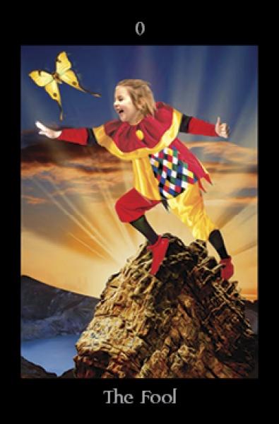 A child jester stands on a rocky peak at sunset, reaching for a yellow butterfly. The Fool card, numbered 0, is a vibrant image from the Pagan Ways Tarot by Schiffer Publishing, Ltd., a unique Pagan-themed tarot deck.