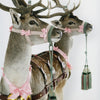 Two deer with pink bows, gold heart ornaments, and green tasseled reins stand against a white background—an image featured in "Humor in Craft" by Schiffer Publishing, Ltd., celebrating the playful spirit of contemporary craft artists.