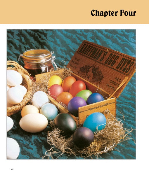 A wooden box labeled "Egg Dyes" holds bright eggs in straw, featuring beeswax designs. Nearby are plain eggs and a jar, all on teal-patterned cloth. Caption: Chapter Four. Product: Decorating Eggs by Schiffer Publishing, Ltd.