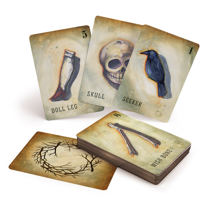 The Between the Worlds oracle deck by Schiffer Publishing, Ltd. features illustrated cards like Doll Leg, Skull, and Seeker, with others such as Wish Bone and a thorny wreath design shown in an eye-catching display.