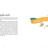 An open book reveals instructions for using the Dream Your Joy Oracle Cards by Schiffer Publishing, Ltd. on the left page, while the right page displays a ribbon that reads "ORACLE CARDS" in bold letters.