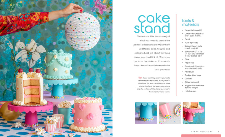 A vibrant party scene showcases three cakes on pastel stands, confetti, a hand with a white paper lantern, and blue floral wallpaper, with text about a DIY cake stand project from Schiffer Publishing, Ltd.'s The Big Book of Happy Crafts.